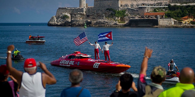 Lucas Oil SilverHook powerboat drivers Nigel Hook, waving a Stars and Stripes, and James Johnson, waving a Cuban national flag, stand aboard their speedboat, backdropped by "El Morro" castle, in Havana, Cuba, Thursday, Aug. 17, 2017. The team led by Hook, a California-based businessman, is claiming a record for a powerboat crossing from Florida to Cuba. The crew reports making it from Key West to Havana on Thursday in 1 hour and 18 minutes. (AP Photo/Ramon Espinosa)