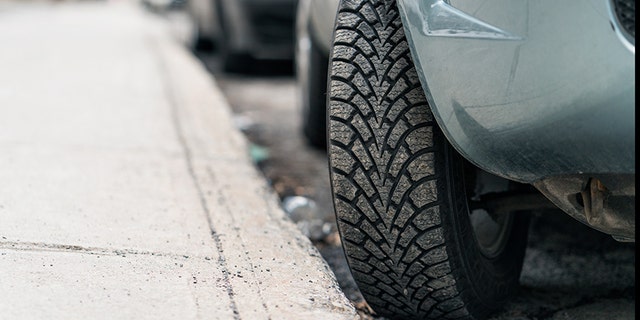 Close-up of a car parked on a hill, with the tire turned into the curb to stop the car from rolling forward.