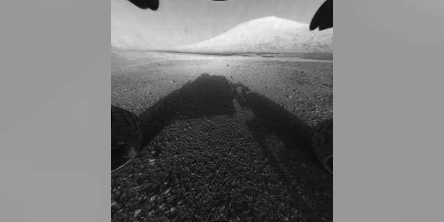 This image taken by NASA's Curiosity shows what lies ahead for the rover -- its main science target, Mount Sharp. The rover's shadow can be seen in the foreground, and the dark bands beyond are dunes.