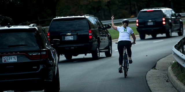 A woman on a bike gestures with her middle finger as a motorcade with US President Donald Trump departs Trump National Golf Course October 28, 2017 in Sterling, Virginia.