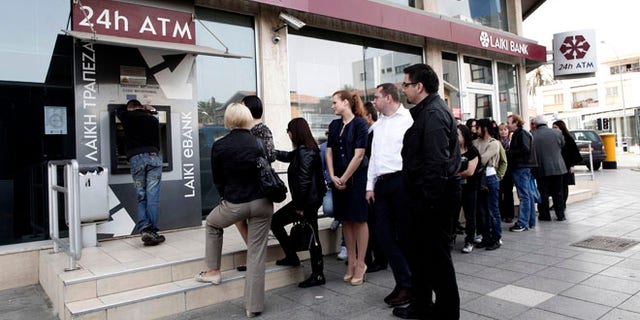 March 21, 2013: People queue at an ATM outside a closed Laiki Bank branch in capital Nicosia, Cyprus. The European Central Bank says it will keep emergency aid for Cyprus' troubled banks in place at least until Monday but will have to cut it off after that unless an international rescue program is drawn up.