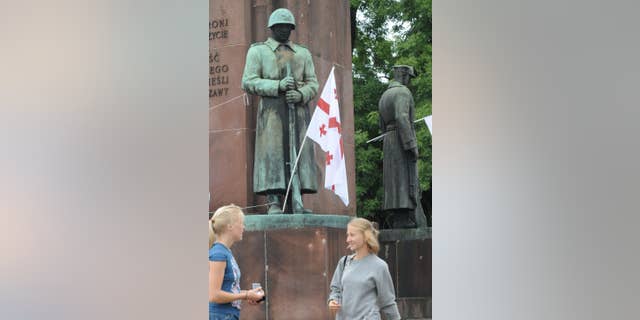 FILE - In this Aug. 13, 2008 file photo people walk past a 1945 monument of Polish-Soviet World War II brotherhood in arms, with Georgian national flags placed on it as a protest against Russia's involvement in Georgia, in Warsaw, Poland. Warsaw city councilors have banned the monument from being returned to its place in a city square, after it was temporarily removed from that square in 2011 to allow for the construction of a subway line in the area. (AP Photo/Alik Keplicz, File)