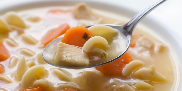 A bowl of chicken noodle soup. Focus is on the front of the spoon.