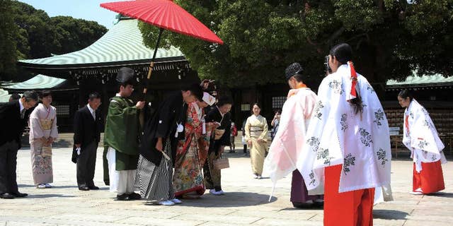 FILE - In this May 27, 2015 file photo, a newlywed couple, center, bows to a Shinto priest, third from right, in the compound of Meiji Jingu Shrine after their Japanese traditional wedding ceremony in Tokyo. In Japan, every marriage costs one surname. The Supreme Court may change that on Wednesday, Dec. 16, 2015. A Civil Code that dates from the 19th century says couples must adopt one surname, and women almost always sacrifice theirs. Five plaintiffs filed a lawsuit in 2011 saying the law is unconstitutional, violates their civil rights and puts the burden almost entirely on women. Two lower courts have ruled against them, setting the stage for Wednesday’s Supreme Court ruling. (AP Photo/Eugene Hoshiko, File)