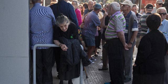 Elderly people, who usually get their pensions at the end of the month, wait outside a closed bank in Athens, Monday, June 29, 2015. Greece's five-year financial crisis took its most dramatic turn yet, with the cabinet deciding that Greek banks would remain shut for six business days and restrictions would be imposed on cash withdrawals. (AP Photo/Petros Giannakouris)
