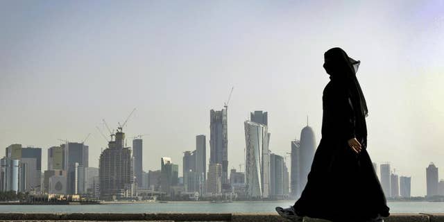 FILE- In this May 14, 2010 file photo, a Qatari woman walks in front of the city skyline in Doha. A lawyer says a Dutch woman who told Qatari police she had been drugged and raped in March has been in government detention ever since on unclear charges. Speaking to The Associated Press, lawyer Brian Lokollo says the 22-year-old woman has appeared three times in court and thinks she may face an adultery charge. (AP Photo/Kamran Jebreili, File)