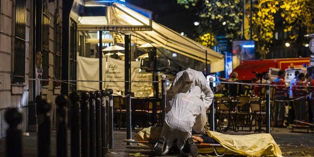 In this Friday, Nov. 13, 2015 file photo of Investigating police officers inspect the lifeless body of a victim of a shooting attack outside the Bataclan concert hall in Paris, France. AP Photo/Kamil Zihnioglu