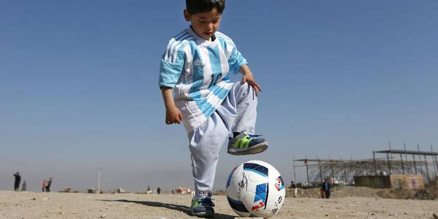 FILE - In this Friday, Feb. 26, 2016 file photo, Murtaza Ahmadi, a five-year-old Afghan Lionel Messi fan plays with a soccer ball during a photo opportunity as he wears a shirt signed by Messi, in Kabul, Afghanistan. The father of Ahmadi says the family was forced to leave Afghanistan amid constant telephone threats. (AP Photo/Rahmat Gul, File)