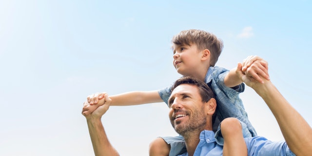 Portrait of happy father giving son piggyback ride on his shoulders and looking up.