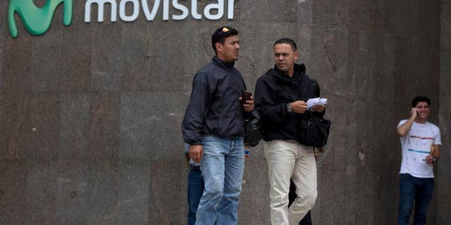 Pedestrians walk outside Movistar a cell phone company office in the Chacao municipality of Caracas, Venezuela, Monday, April 11, 2016. Movistar, a subsidiary of the Spanish-based Telefonica, and Digitel both announced last week that they would be cutting international service because of issues related to Venezuela's byzantine currency controls. (AP Photo/Fernando Llano)