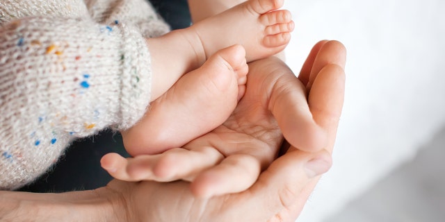 Baby feet in father hands. Tiny Newborn Baby's feet on male shaped hands closeup. Dad and his Child. Happy Family concept.