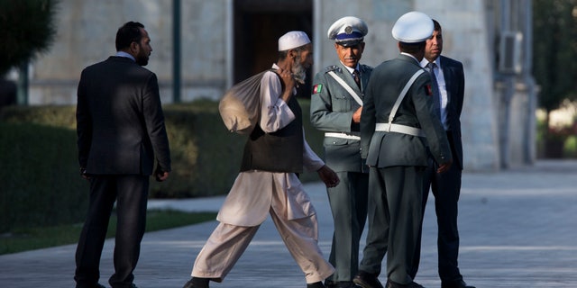 A worker walks past Afghan guards as they wait for a news conference that has been delayed between U.S. Secretary of State John Kerry and Afghan President Hamid Karzai at the presidential palace on the second day of an unannounced stop in Kabul, Afghanistan, on Saturday, Oct. 12, 2013. Kerry extended talks Saturday with Karzai on a bilateral security agreement with the United States, and while work remains to be done a deal could be struck by the end of the day, a presidential spokesman said. (AP Photo/Jacquelyn Martin, Pool)