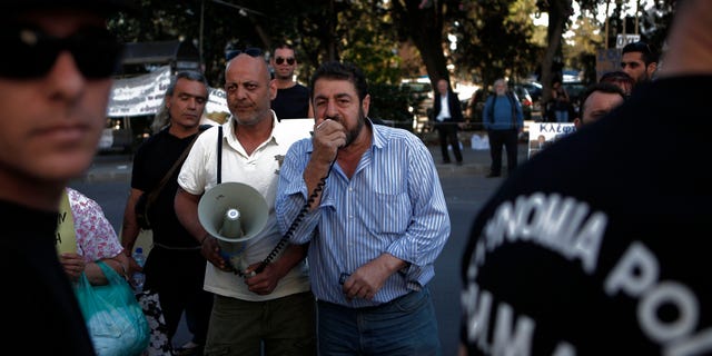 Protesters shout slogans behind riots police, during an anti-bailout protest outside of the Cyprus' parliament, in capital Nicosia, Thursday, April 25, 2013. Cyprus’ central bank says the Romanian operations of the island nation’s largest lender Bank of Cyprus will resume April 26th after being suspended for more than three weeks amid plans to sell them off. (AP Photo/Petros Karadjias)