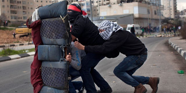 FILE - In this Feb. 19, 2013 photo, masked Palestinians use a rear car seat as a shield during a protest to support Palestinian prisoners, outside Ofer, an Israeli military prison near the West Bank city of Ramallah. Senior Palestinians say the diplomatic pressure that produced the nuclear deal with Iran, world powers negotiating jointly and wielding the stick of sanctions, should now be applied to the long-festering Israeli-Palestinian conflict. (AP Photo/Bernat Armangue, File)