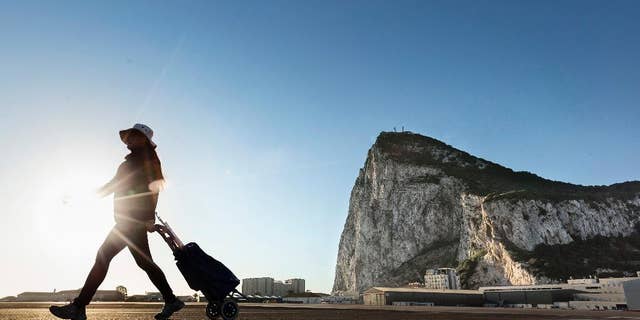 FILE- In this Wednesday, March 1, 2017 file photo, a woman walks on the Spanish side of the border between Spain and the British overseas territory of Gibraltar with the Rock of Gibraltar in the background, in La Linea de la Concepcion, Spain. Deep inside the Rock of Gibraltar is a room known as The Vault. Dug by the British army in World War Two, the room now houses servers that power the websites of dozens of international online gambling companies. Those companies were lured to this speck of British territory on Spain's southern tip by its low taxes and its unimpeded access to the European Union's single market of around 500 million people. Britain's looming departure from the EU, therefore, has cast a cloud over Gibraltar's future because Brexit could see it shut off from the rest of the EU.(AP Photo/Daniel Ochoa de Olza, File)