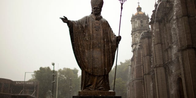 A statue of Pope John Paul II stands outside the Basilica of Guadalupe during heavy rain in Mexico City, Friday, July 5, 2013. Pope Francis on Friday approved the miracle of a Costa Rican woman bringing John Paul to the ranks of saints. Floribeth Mora suffering from a cerebral aneurysm and only given a month to live, was inexplicably cured on May 1, 2011, the date of John Paul's beatification, when millions of worshippers filled St. Peter's Square to honor the beloved Polish pontiff. (AP Photo/Ivan Pierre Aguirre)