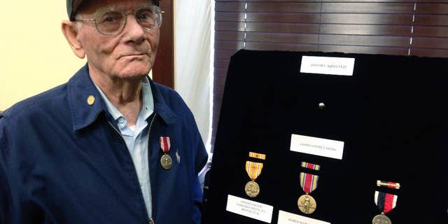 World War II veteran Joseph Aquilante, 91, of North Providence, R.I., stands beside medals presented to him by U.S. Sen. Jack Reed, Monday, May 15, 2017, at the senator's office in Cranston, R.I. Joseph Aquilante, of North Providence, sought the medals so he could leave them for his grandchildren and great-grandchildren. He says he wants to pass them on as a keepsake and part of history. (AP Photo/Jennifer McDermott)