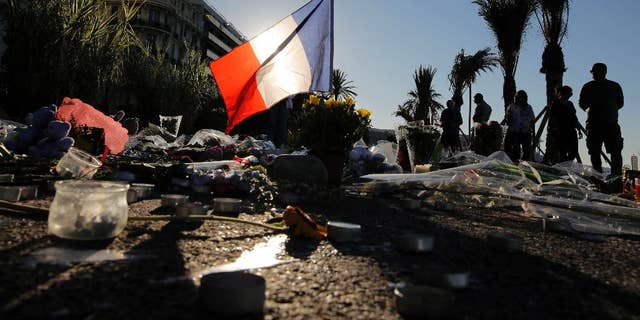 FILE - In this Sunday, July 17, 2016 file photo, a French flag stands among a floral tribute for the victims killed during a deadly attack, on the famed Boulevard des Anglais in Nice, southern France. Residents of the French Riviera city of Nice that lived through the truck rampage horror in July 2016, are reliving it this week following a chillingly similar narrative in Berlin. (AP Photo/Laurent Cipriani, File)