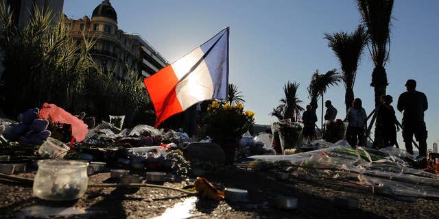 FILE - In this Sunday, July 17, 2016 file photo, a French flag stands among a floral tribute for the victims killed during a deadly attack, on the famed Boulevard des Anglais in Nice, southern France. Residents of the French Riviera city of Nice that lived through the truck rampage horror in July 2016, are reliving it this week following a chillingly similar narrative in Berlin. (AP Photo/Laurent Cipriani, File)