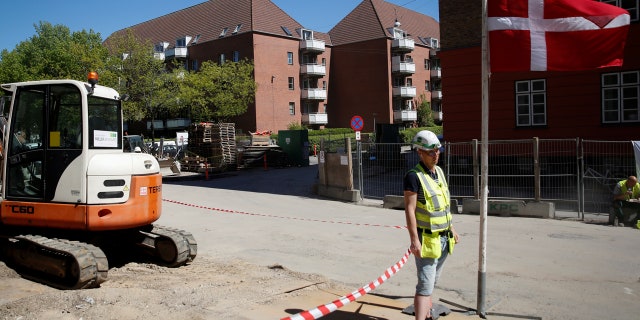 A worker stands beside a Danish flag on a construction site of new housing being built next to Mjolnerparken, a housing estate that features on the Danish government's "Ghetto List", in Copenhagen, Denmark, May 8, 2018.