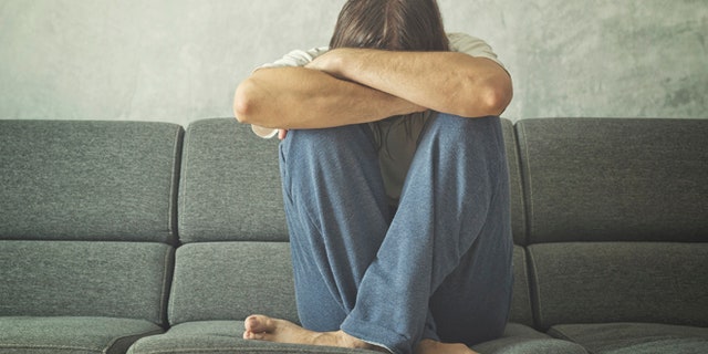 Depressed and sad man on the couch in the room, covering face and crying in despair.