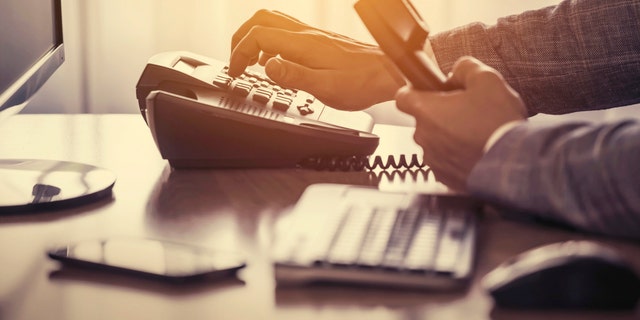 Businessman use the phone in the office, keyboard, mouse, mobile, and monitor detail in the background