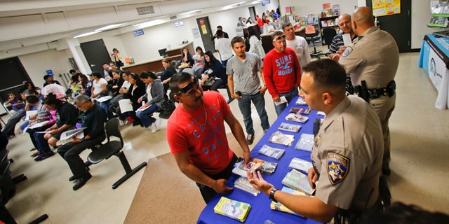FILE - In this Wednesday, April 23, 2014 file photo, California Highway Patrol officers Armando Garcia, right, and Ray Patton explain to immigrants the process of getting a drivers license during an information session at the Mexican Consulate, in San Diego. California is gearing up to start issuing driverâs licenses to immigrants in the country illegally in a bid to make the roads safer that could also give more than a million people access to state-issued identification. (AP Photo/Lenny Ignelzi,File)