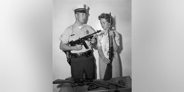 In this 1961 photo, Tucson Police Sgt. Tom Keeley holds a Colt Thompson submachine gun and secretary Linda Bradfield holds a Winchester Model 1907, with other guns confiscated from the John Dillinger gang during Dillinger's capture in Tucson, Ariz., in 1934