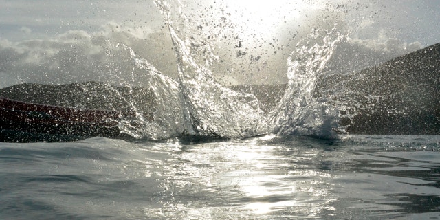 View of a splash at water level after someone jumped into the sea with sun in the background