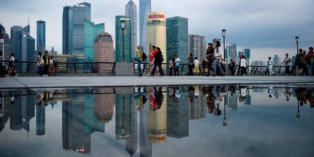Pedestrians walk past the skyline of the city's financial district in Shanghai on October 8, 2010.