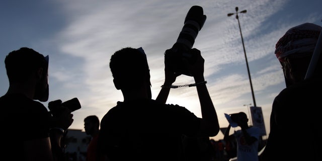 Masked Bahraini anti-government protesters wearing handcuffs hold cameras up to show support for jailed photographers during a march in Saar, Bahrain, on Friday, Dec. 13, 2013. Thousands participated in the march organized by opposition parties to mark 1,000 days since the pro-democracy uprising began in the Gulf island kingdom. As the peaceful march dispersed, a group of masked youths confronted riot police nearby, igniting clashes. (AP Photo/Hasan Jamali)