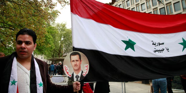 A Syrian supporting the regime of Syrian President Bashar Assad, holds a placard with his picture and the national flag as he participates in a protest outside the US Embassy in central London, Saturday, May 18, 2013. (AP Photo/Lefteris Pitarakis)