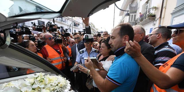 Members of the media crowd around the hearse of Tiziana Cantone as her mother Teresa Giglio, center, salutes it, during her funeral in Casalnuovo, near Naples, Italy, Thursday, Sept. 15, 2016. Italian prosecutors in Naples have opened an investigation into possible charges of instigation to suicide after a 31-year-old woman killed herself after failing in a long legal battle to get a pornographic video removed from the Internet.  (Ciro Fusco/ANSA via AP)