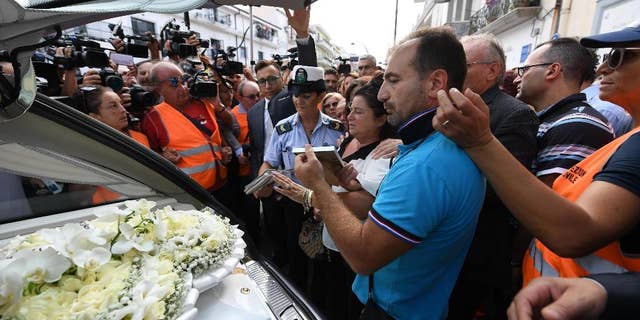 Members of the media crowd around the hearse of Tiziana Cantone as her mother Teresa Giglio, center, salutes it, during her funeral in Casalnuovo, near Naples, Italy, Thursday, Sept. 15, 2016. Italian prosecutors in Naples have opened an investigation into possible charges of instigation to suicide after a 31-year-old woman killed herself after failing in a long legal battle to get a pornographic video removed from the Internet. (Ciro Fusco/ANSA via AP)