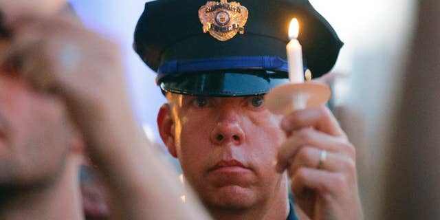 A police officers takes part in a candle light vigil at City Hall, Monday, July 11, 2016, in Dallas. Five police officers were killed and several injured during a shooting in downtown Dallas last Thursday night. (AP Photo/Tony Gutierrez)