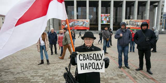 A protester holds a poster reading 'Freedom for the people' and an old Belarus flag, a symbol of protest, during an opposition rally in Minsk, Belarus, Monday, May 1, 2017. The protesters marched through central Minsk calling for the government to step down and for free elections to be held. (AP Photo)