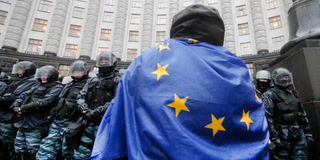 An opposition supporter draped in an EU flag, attends a protest in front of the Ukrainian Cabinet of Ministers in Kiev, Ukraine, Monday, Nov. 25, 2013. Hundreds of angry Ukrainians on Monday clashed with riot police outside the government building as protests continued in Kiev over the government’s abrupt decision to pause integration with the West and tilt toward Moscow. The scuffle Monday morning follows a large protest in the heart of Kiev Sunday, the biggest since the 2004 Orange Revolution that brought a pro-Western government to power. Tens of thousands of people turned up to protest President Viktor Yanukovych’s decision to snub a potentially historic deal with the EU and focus on ties with Moscow, after immense pressure from Russia. (AP Photo/Efrem Lukatsky)