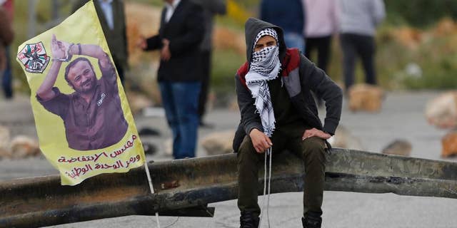 FILE -- In this April 23, 2017 file photo, a Palestinian protester holds a sling shot as he sits near a banner with a picture of jailed leader Marwan Barghouti that reads, "The architect of the uprising," following a protest supporting prisoners in Israeli jails, in the West Bank city of Ramallah. An Israeli official said Monday, May 1, 2017, that the number of Palestinians prisoners participating in one of the largest hunger strike in years dropped to 870, from 1,300 a week earlier. Support for the hunger strikers who seek better conditions has gained momentum with West Bank marches and a social media campaign and has boosted the Palestinian leadership credentials of its imprisoned organizer, Barghouti. (AP Photo/Majdi Mohammed, File)