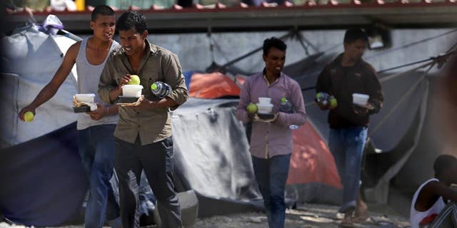 Migrants carry food at the Moria refugee camp on the northeastern Greek island of Lesbos, on Tuesday, Sept. 20, 2016, after a fire gutted the camp following protests at the camp. Authorities of the island of Lesbos are calling for the immediate evacuation of thousands of refugees to the Greek mainland, following the fire and nine migrants suspected of starting the blaze have been arrested, authorities said Tuesday. (Dimitris Tosidis/InTime News via AP)