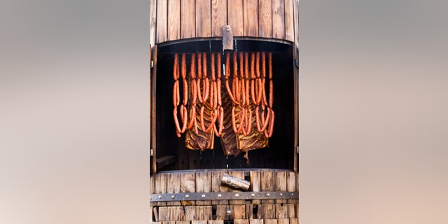 sausages and bacon being smoked in barrel-shaped smoker