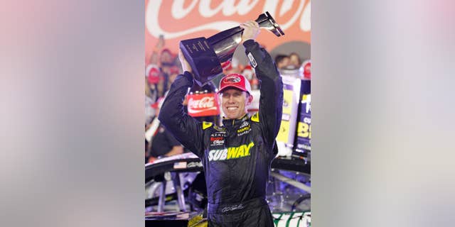 Carl Edwards raises the trophy in Victory Lane after winning the NASCAR Sprint Cup series auto race at Charlotte Motor Speedway in Concord, N.C., Sunday, May 24, 2015. (AP Photo/Terry Renna)
