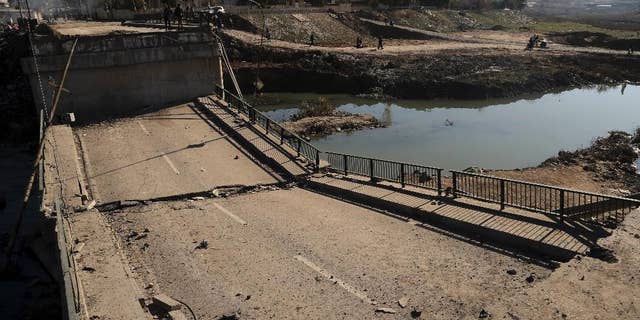 People inspect a bridge destroyed by Islamic State militants in a neighborhood recently liberated from Islamic State on the eastern side of Mosul, Iraq, Thursday, Jan. 12, 2017. Small stalls and carts have sprung up outside the bombed-out restaurants and cafes in eastern Mosul, selling fresh vegetables, cigarettes and cellphones to the thousands of civilians still living in neighborhoods where the Iraqi military has driven out the extremists of the Islamic State group.(AP Photo/ Khalid Mohammed)