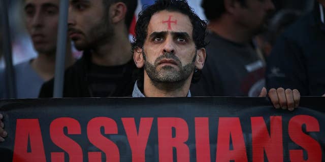 FILE - In this Saturday, Feb. 28, 2015 file photo, an Assyrian man with a red cross painted on his forehead holds a banner as he walks during a protest of several hundred people in solidarity with Christians abducted in Syria and Iraq, in downtown Beirut, Lebanon. Activists said on Saturday, March. 7, 2015, that Islamic State militants have attacked a string of predominantly Christian villages in northeastern Syria, touching off heavy clashes with Kurdish militiamen and their local allies. (AP Photo/Hussein Malla, File)