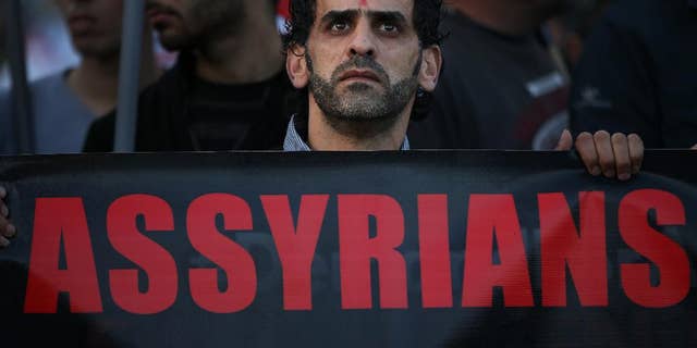 FILE - In this Saturday, Feb. 28, 2015 file photo, an Assyrian man with a red cross painted on his forehead holds a banner as he walks during a protest of several hundred people in solidarity with Christians abducted in Syria and Iraq, in downtown Beirut, Lebanon. Activists said on Saturday, March. 7, 2015, that Islamic State militants have attacked a string of predominantly Christian villages in northeastern Syria, touching off heavy clashes with Kurdish militiamen and their local allies. (AP Photo/Hussein Malla, File)