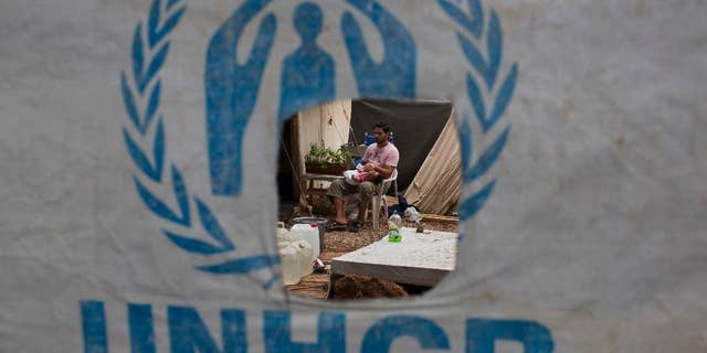 A Syrian man feeds his child behind a UNHCR plastic sheet at Ritsona refugee camp, north of Athens, which hosts about 600 refugees and migrants on Sept. 8, 2016. (AP Photo/Petros Giannakouris)