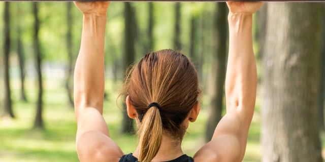 Back view of female doing pull ups outdoors