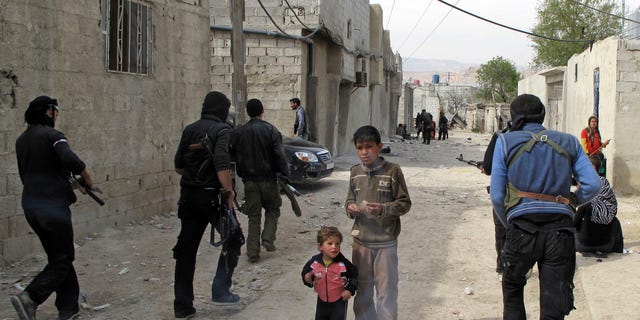 April 1, 2012: Syrian boys watch Free Syrian Army fighters move through a neighborhood of Damascus, Syria.