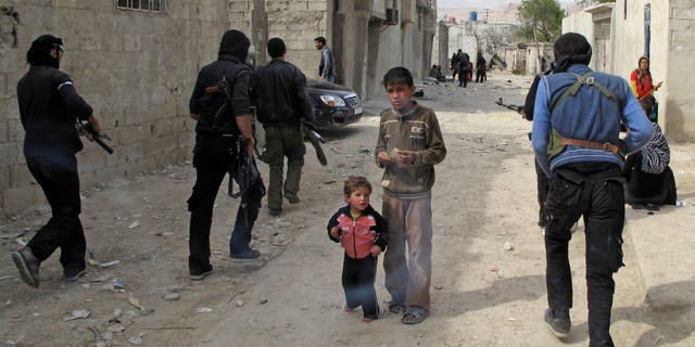 April 1, 2012: Syrian boys watch Free Syrian Army fighters move through a neighborhood of Damascus, Syria.