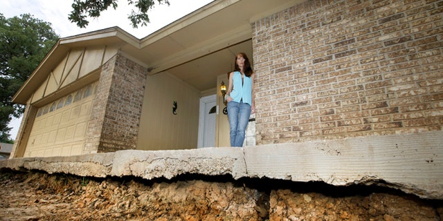 June 21, 2014: Barbara Brown poses for a photo on the front step of her home that now sits about one foot off the surface of her lawn.