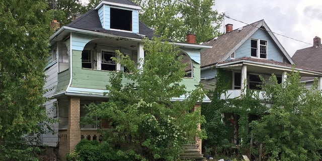 This Aug. 31, 2016, photo shows houses with missing windows and overgrown lawns along a street marred by cracks and potholes in East Cleveland, Ohio. Cleveland and East Cleveland, two of the country's poorest cities, are debating whether to merge, with both cities saying the state of Ohio needs to provide millions to begin fixing East Cleveland's infrastructure and finances.